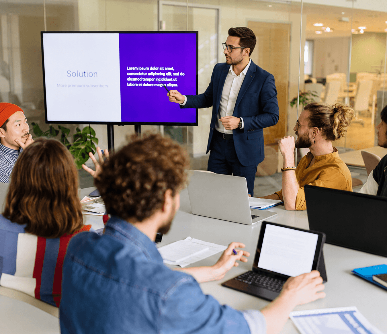 Business professional delivering a digital presentation titled Solution to a creative team in an open-plan office boardroom.